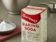 Imagen of A box of baking soda with a red and white label sitting on a counter next to a measuring cup